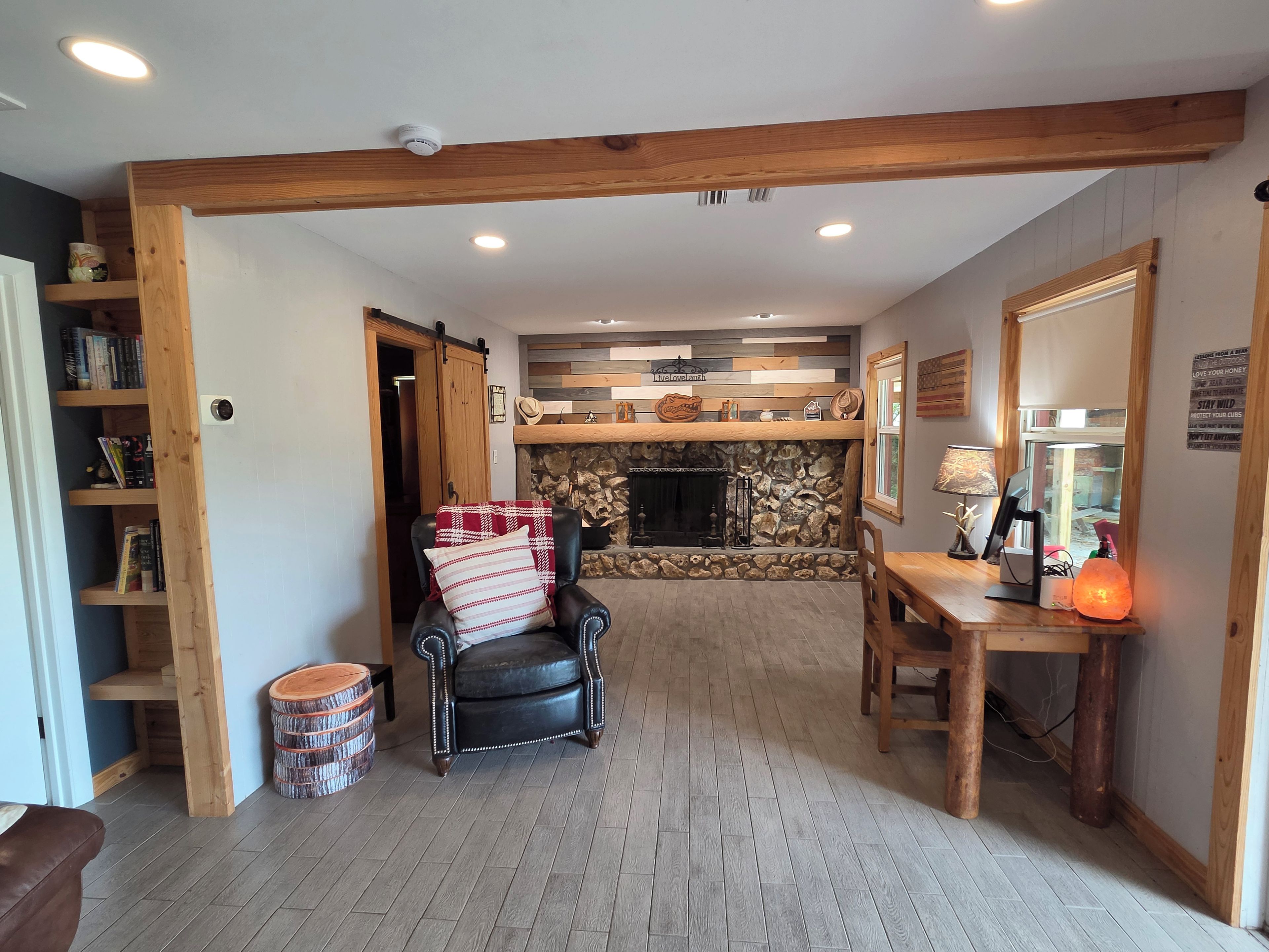 A cozy living room with a fireplace, a leather armchair, a wooden dining table, and a bookshelf.