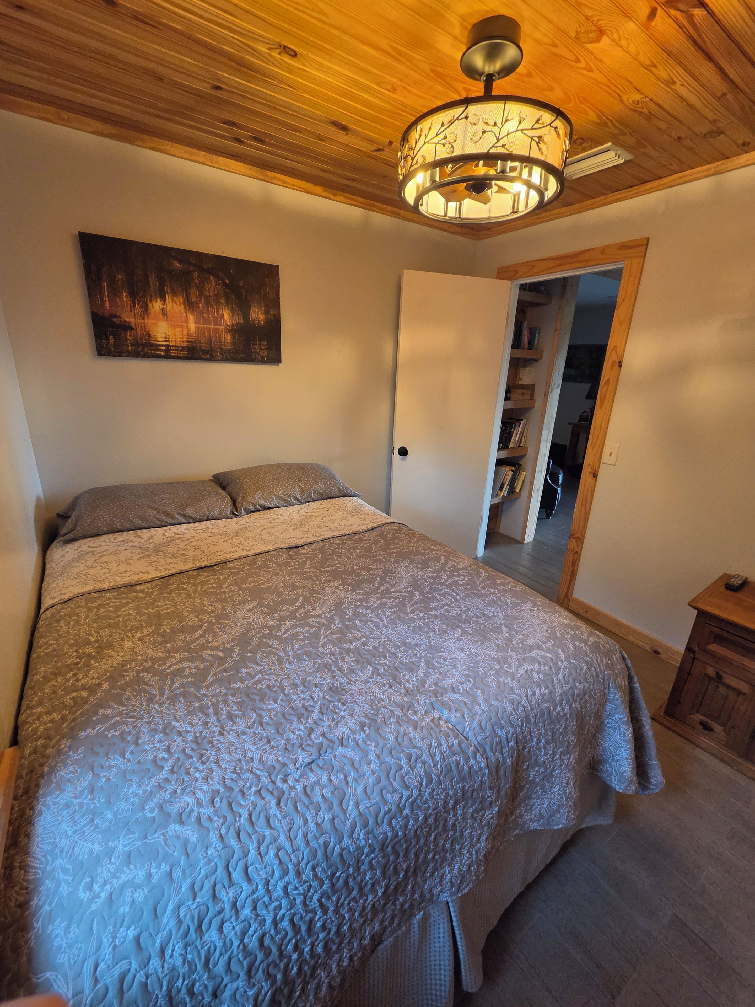 Et soveværelse med en seng, ventilator, et billede og en dør, der fører til en gang.