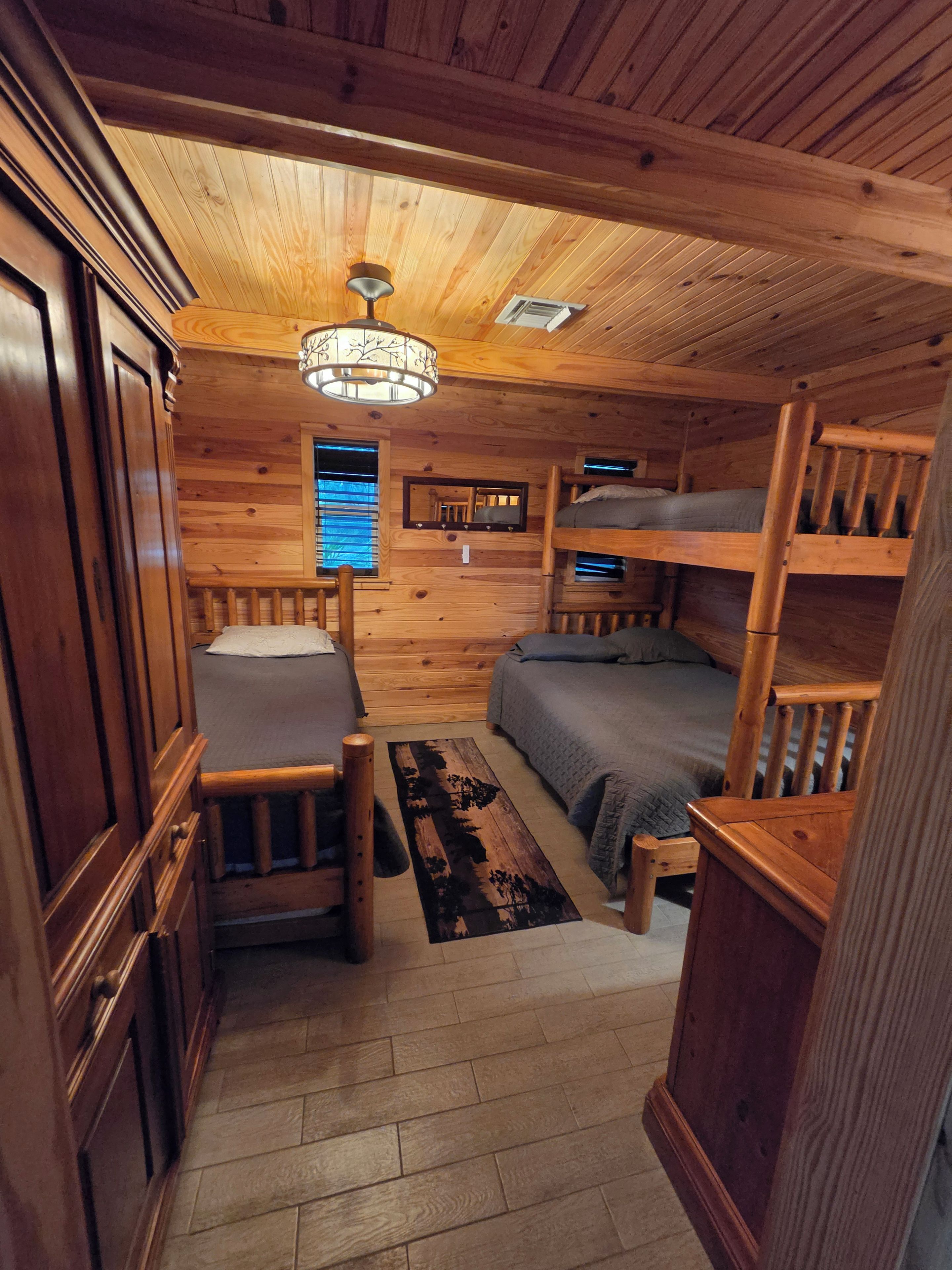 A compact cabin with a bunk bed, a single bed, a desk, and a mirror.