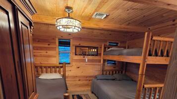 A compact cabin with a bunk bed, a single bed, a desk, and a mirror.