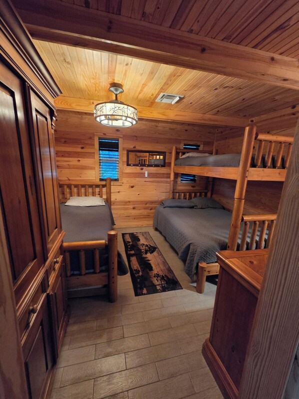 A compact cabin with a bunk bed, a single bed, a desk, and a mirror.