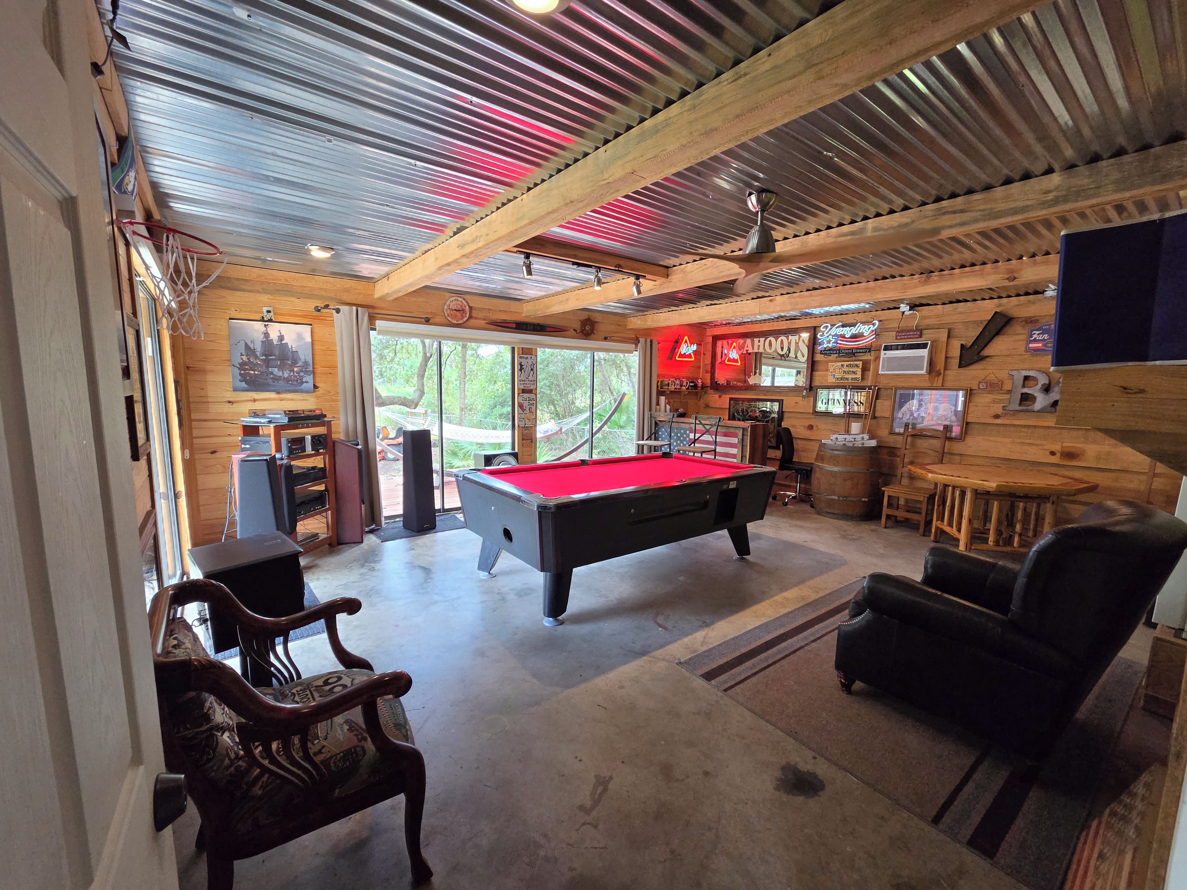 A pool table in a room with wooden walls and a ceiling with corrugated metal.