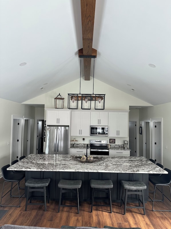 A modern kitchen with a large island, stainless steel appliances, and a wooden ceiling.