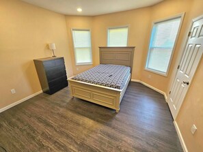 A bedroom with a bed, dresser, and windows.