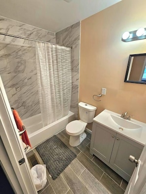 A bathroom with a shower, toilet, sink, and marble walls.