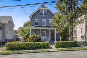 A two-story residential house with a front porch, a small front yard, and a street view.