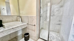 Ein Badezimmer mit Marmorwaschbecken, einer Duschkabine aus Glas und einem Mülleimer.