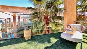Ein Balkon mit Glasgeländer, einem weißen Stuhl, einem gewebten Korb und einem Blumentopf.