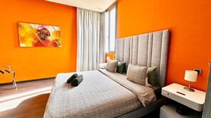 Ein modernes Hotelzimmer mit einem großen Bett, einem Nachttisch, einer Lampe und einem mit Vorhängen versehenen Fenster.