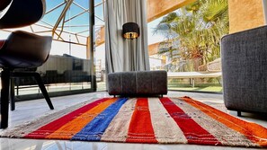Ein modernes Wohnzimmer mit einem großen Fenster, einem grauen Sofa, einem farbenfrohen Streifen Teppich und einer schwarzen Lampe.
