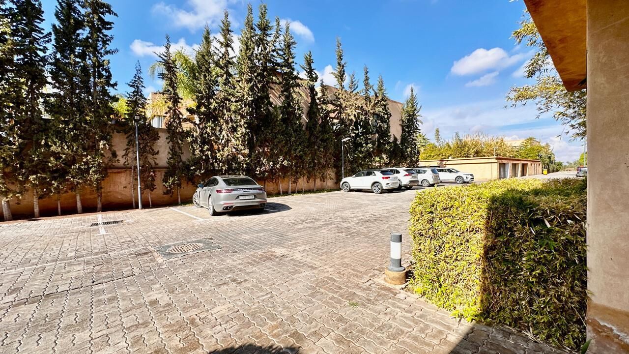 A parking area with paved ground, a white car, and a building in the background.