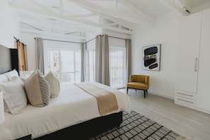 A modern bedroom with a large bed, a chair, and a view through the window. - Stunningly decorated home with breathtaking views! (Helensvale)