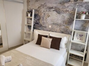 A neatly made bed with white and brown pillows, a white headboard, and a marble-patterned wall behind it. - Villa de blue 3 (Bol)