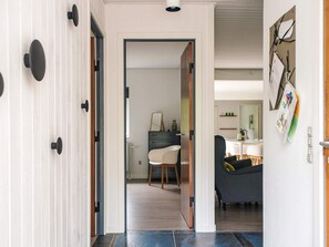 A hallway with a wooden door, a white wall with a bulletin board, and a dining area with a table and chairs. - 5 Star Holiday Home in Farvang (Farvang)