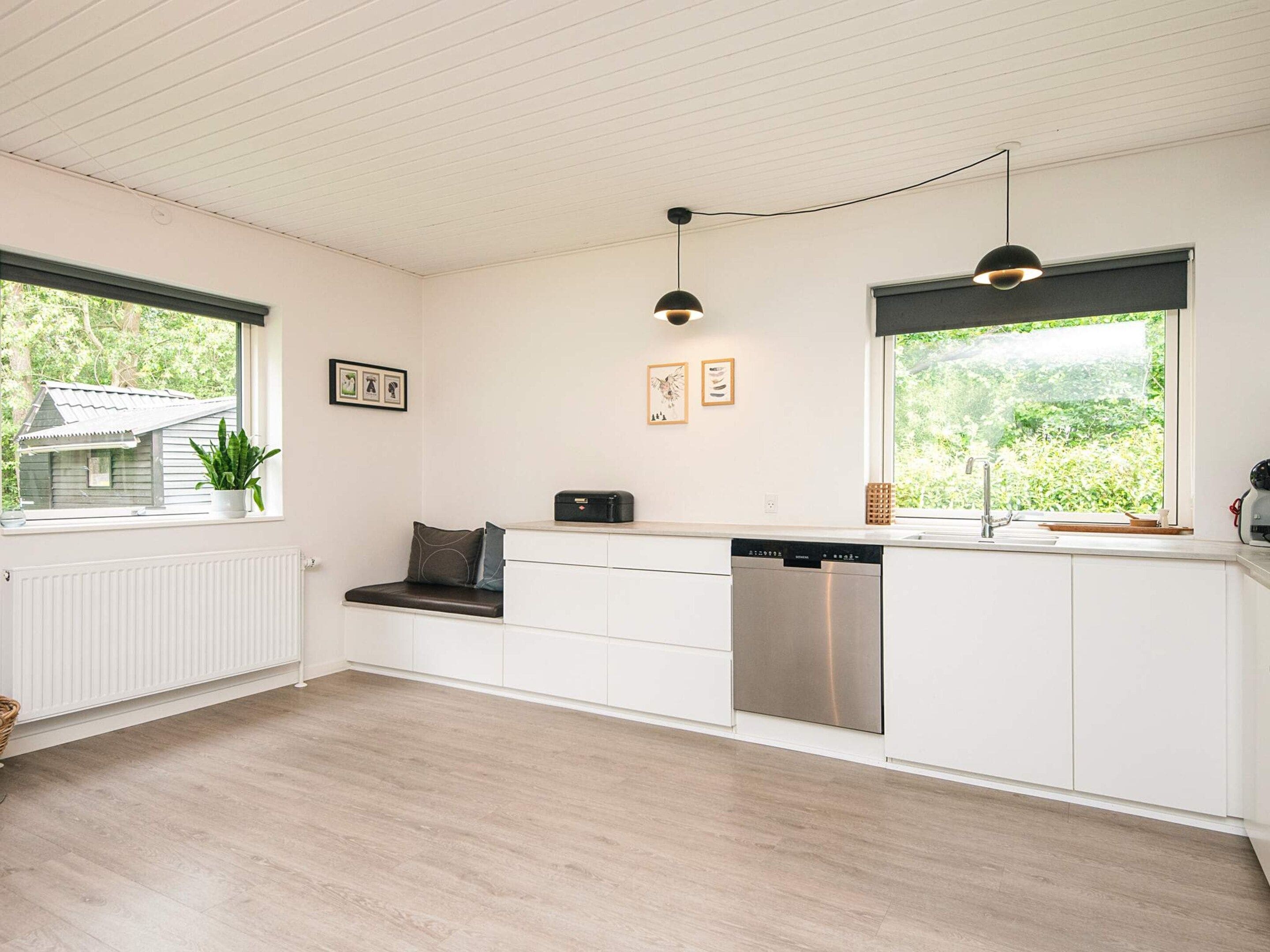 Een moderne keuken met witte kasten, een inbouw vaatwasser en een raam met uitzicht op groen.
