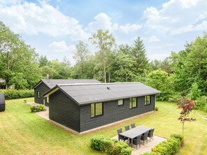 A modern two-story house with a dark exterior, a sloped roof, and a small front yard with a table and chairs. - 5 Star Holiday Home in Farvang (Farvang)