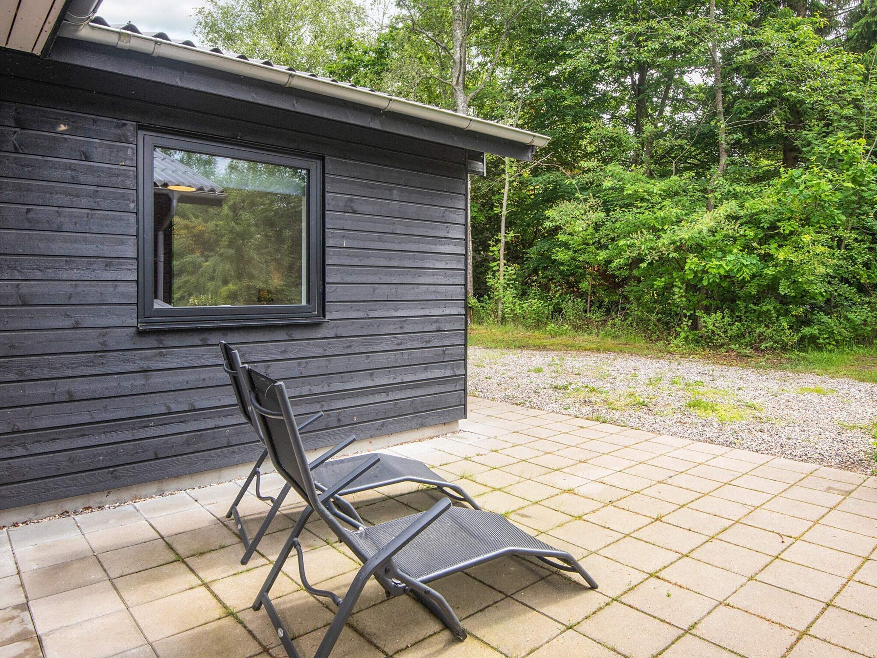 A wooden cabin with a window and a patio area with two chairs.