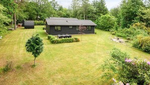 Ein modernes Haus mit gepflegtem Rasen, umgeben von dichten Bäumen und Sträuchern.