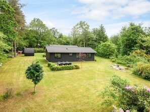 A modern house with a well-maintained lawn, surrounded by dense trees and shrubs. - 5 Star Holiday Home in Farvang (Farvang)