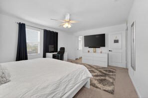 A bedroom with a bed, a desk, a chair, a television, and a ceiling fan. - Blue Yard Homes • 4BR Near JBSA Randolph • Hot Tub & PS5 (Converse)