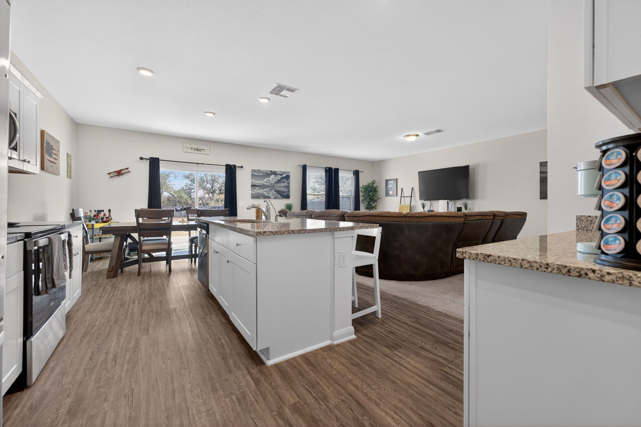 A modern kitchen with white cabinetry, a central island, and a dining area with a brown leather couch.