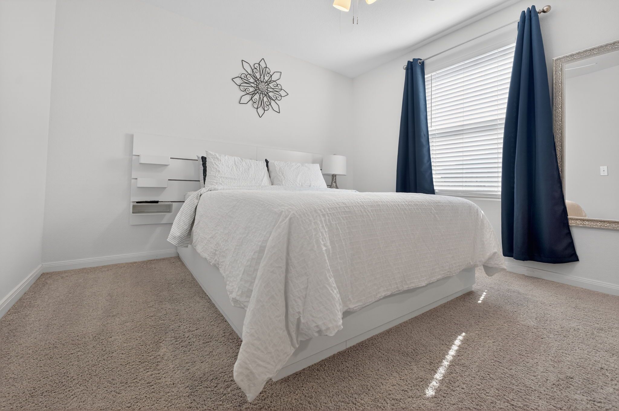 Une chambre à coucher avec un lit, un élément décoratif fixé au mur, une fenêtre avec des rideaux et un sol recouvert d’une moquette.