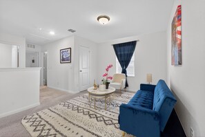 A living room with a blue sofa, a round coffee table, a white chair, and a patterned rug. - Blue Yard Homes • 4BR Near JBSA Randolph • Hot Tub & PS5 (Converse)