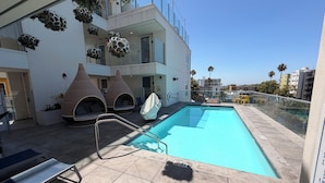 A rooftop pool area with a clear blue pool, lounge chairs, and a view of the city skyline. - Chic Urban Luxury Retreat 1Bedroom Apartment (Los Angeles)