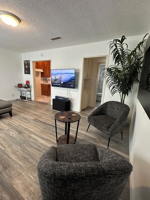 Ein modernes Wohnzimmer mit Flachbildfernseher, einem Essbereich mit Holzschränken und einer großen Topfpflanze.