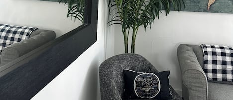Une pièce avec un canapé gris, un fauteuil avec un coussin noir, un grand miroir et une carte du monde accrochée au mur.