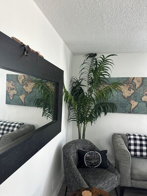 A room with a grey sofa, a chair with a black pillow, a large mirror, and a world map on the wall. - Stadium Stay! Cozy 2BR Steps from SoFi & Kia Forum (Inglewood)