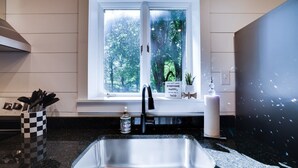 Una cocina con un lavamanos de acero inoxidable, una ventana con vista a árboles, una taza de cuadros y un letrero con una cita.