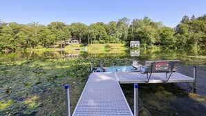 Un muelle con un letrero de advertencia, un bote y casas en un lago rodeado de árboles.