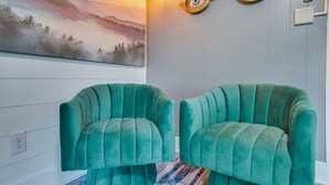 Una habitación con dos sillones color turquesa, un aplique de pared y un cuadro de un paisaje montañoso.