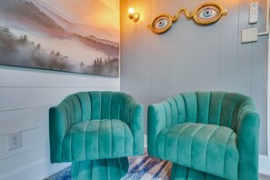 Ein Zimmer mit zwei smaragdgrünen Sesseln, einer Wandleuchte und einem Gemälde einer Berglandschaft.