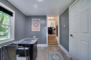 Ein Zimmer mit einem Tisch, Stühlen, einer Heizung, einer Tür und einer Treppe, die in ein weiteres Zimmer führt.