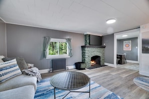 Una sala de estar con chimenea, un sofá, una mesa redonda y una ventana con cortinas.