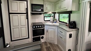 A compact RV kitchen with a stove, oven, microwave, and a sink.