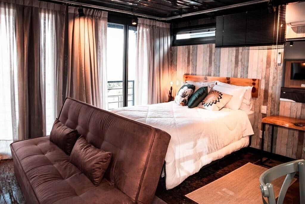 Un dormitorio con una cama grande, un sofá, un televisor y un ventanal con cortinas.