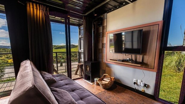 A living room with a sofa, a television, a fireplace, and a large window offering a view of the outdoors.