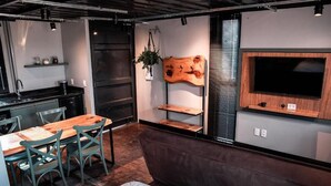 A modern kitchen with a wooden table and chairs, a built-in TV, and a seating area with a sofa and cushions.