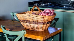 A wicker basket with a red and white checkered cloth on a wooden table in a kitchen with green cabinets and a black countertop.