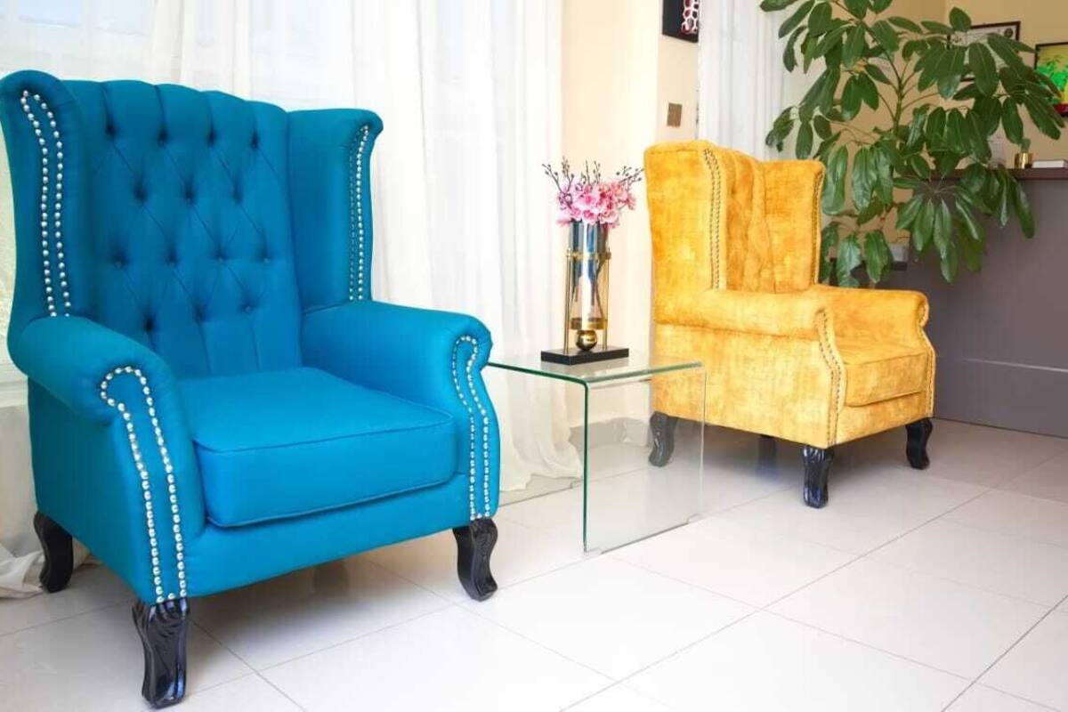 A blue armchair and a yellow armchair in a room with a glass coffee table, a plant, and a reception desk.