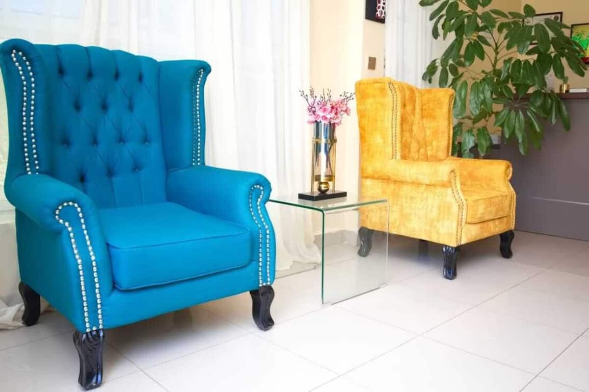 Un fauteuil bleu et un fauteuil jaune se trouvent dans une pièce où l’on aperçoit une table basse en verre, une plante et un comptoir d’accueil.
