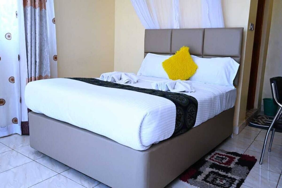 A bed with a white mattress, grey headboard, and a yellow pillow.