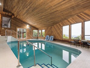 Une piscine intérieure avec un revêtement mural en bois, un escalier et une vue sur l’extérieur.