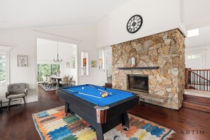 Une table de billard dans une pièce dotée d’une cheminée en pierre, d’un coin repas et d’un escalier.