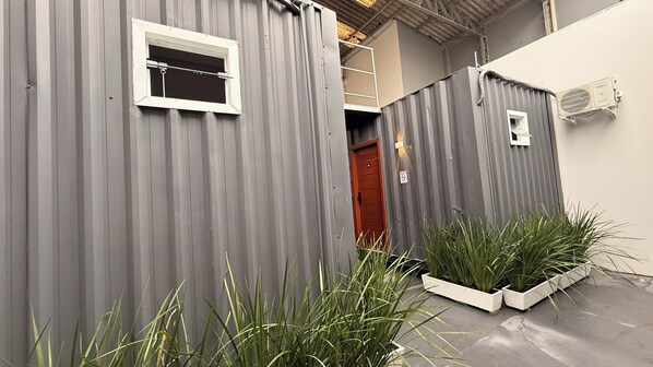 A corrugated metal structure with a window and a door, surrounded by potted plants. - LOFT127 - 04 (Itajaí)