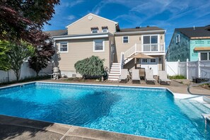 Ein Schwimmbad mit einem Haus im Hintergrund, einer überdachten Terrasse und einem weißen Zaun.