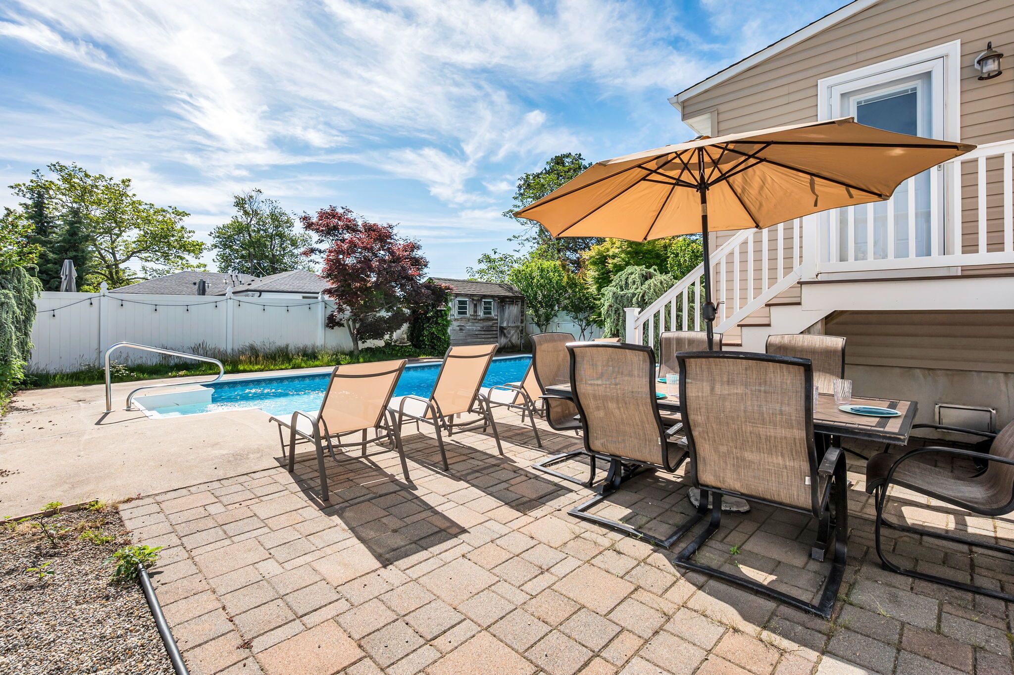 Un jardin avec une piscine, des chaises longues, une table et un parasol.